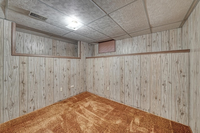 empty room featuring carpet flooring, a drop ceiling, and wood walls