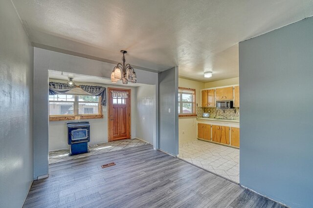 kitchen with decorative backsplash, light wood-type flooring, a textured ceiling, an inviting chandelier, and a wood stove