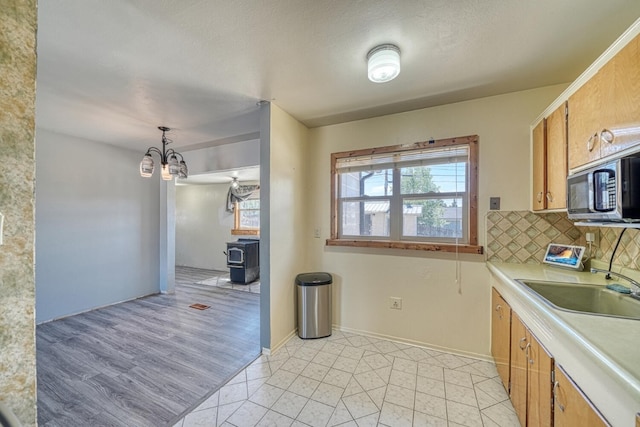 kitchen featuring a wood stove, sink, a notable chandelier, backsplash, and pendant lighting