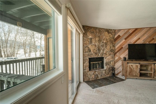 unfurnished living room featuring carpet, wood walls, and a stone fireplace