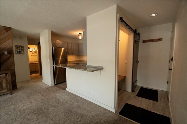 kitchen featuring light carpet, dark stone counters, a barn door, kitchen peninsula, and stainless steel refrigerator