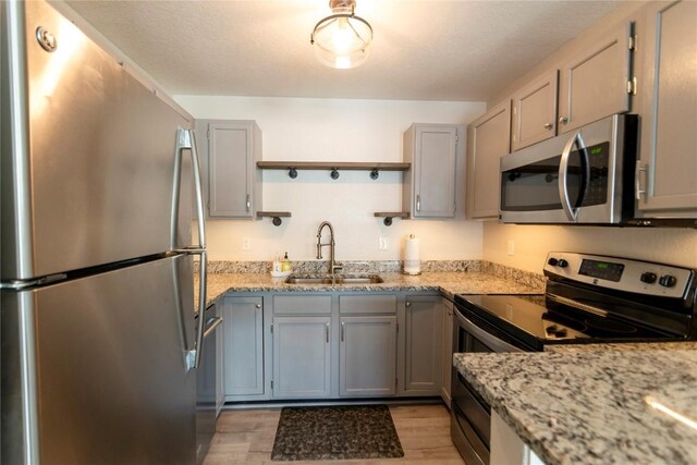 kitchen featuring light stone countertops, light wood-type flooring, gray cabinetry, stainless steel appliances, and sink