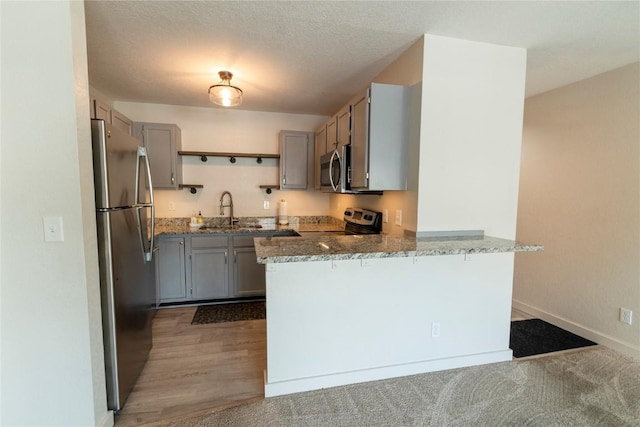 kitchen featuring sink, light stone countertops, a textured ceiling, kitchen peninsula, and stainless steel appliances