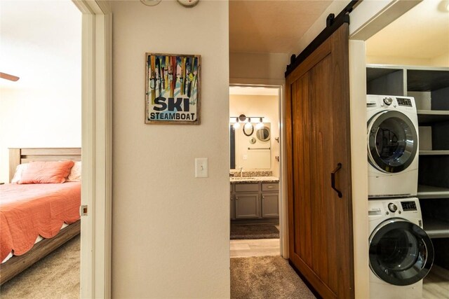 washroom featuring light carpet, a barn door, stacked washer and clothes dryer, and sink