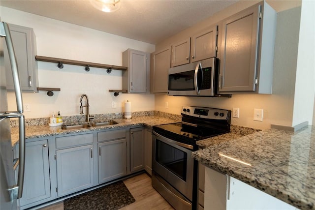 kitchen featuring gray cabinetry, sink, stainless steel appliances, dark stone counters, and light hardwood / wood-style floors