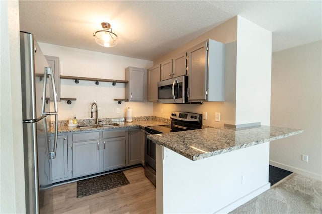 kitchen with kitchen peninsula, gray cabinetry, stainless steel appliances, sink, and stone counters