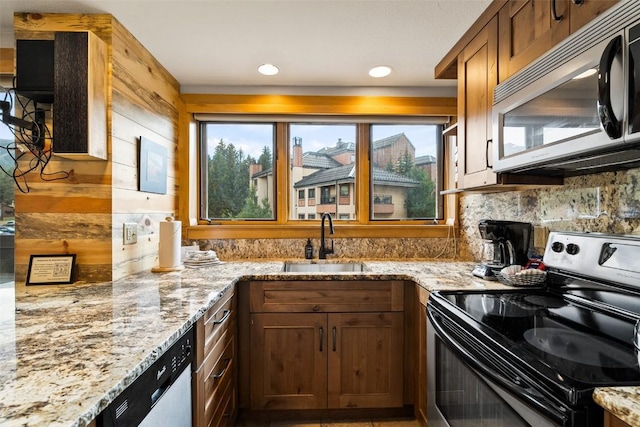 kitchen featuring light stone countertops, sink, wood walls, decorative backsplash, and appliances with stainless steel finishes