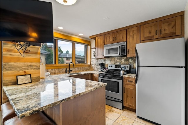 kitchen with sink, kitchen peninsula, white fridge, stainless steel range with electric stovetop, and a breakfast bar