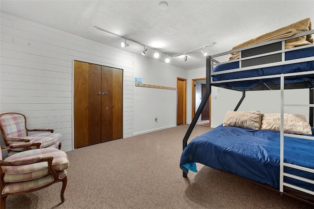 carpeted bedroom featuring a textured ceiling, rail lighting, and wooden walls