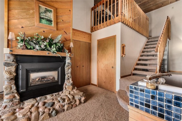 carpeted living room featuring a stone fireplace, wooden walls, a towering ceiling, and wooden ceiling