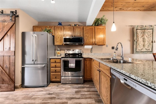 kitchen with light wood-type flooring, stainless steel appliances, sink, a barn door, and decorative light fixtures