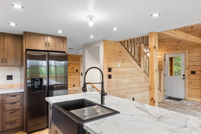 kitchen with stainless steel refrigerator with ice dispenser, light stone counters, wooden walls, sink, and a kitchen island