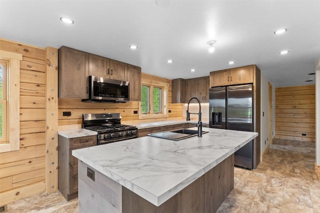 kitchen featuring a center island with sink, sink, stainless steel appliances, and wooden walls