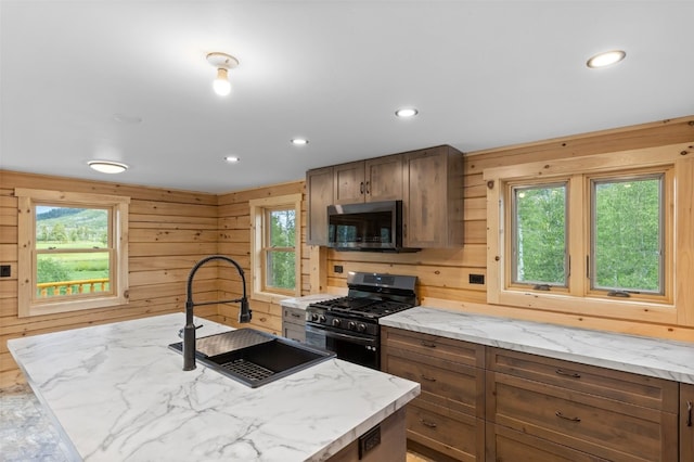 kitchen featuring stainless steel appliances, a wealth of natural light, wooden walls, and sink