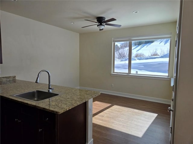 kitchen featuring light stone counters, dark wood-style flooring, a sink, ceiling fan, and baseboards