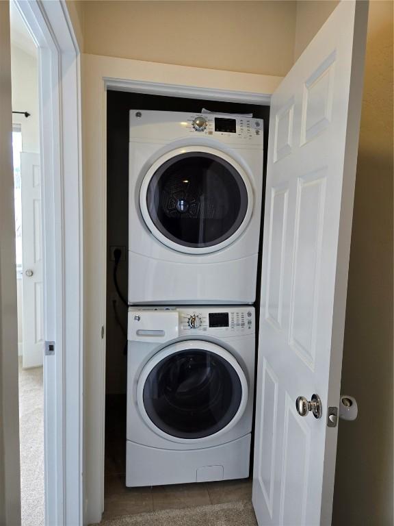 clothes washing area with tile patterned floors, stacked washer and clothes dryer, and laundry area