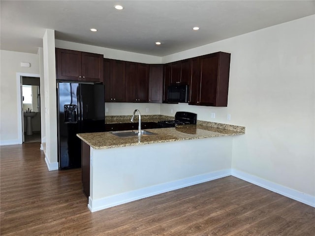 kitchen with a peninsula, black appliances, dark wood-type flooring, and a sink