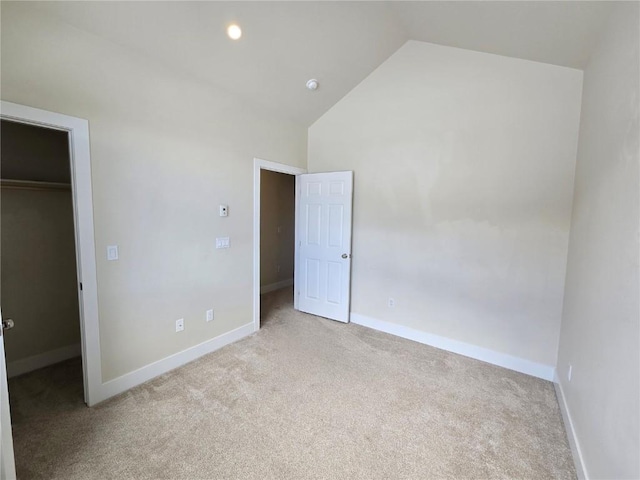 unfurnished bedroom featuring baseboards, light colored carpet, a walk in closet, high vaulted ceiling, and a closet