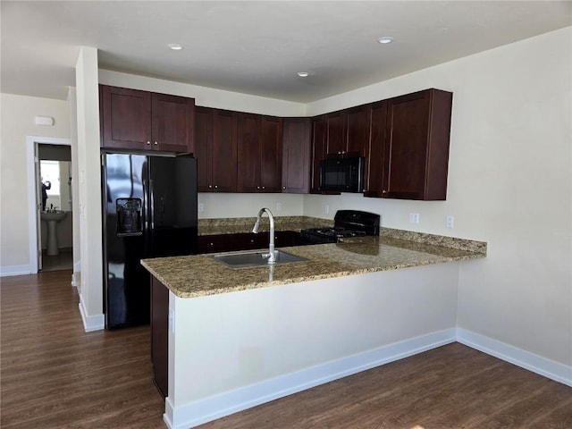 kitchen with dark wood-style flooring, a sink, black appliances, a peninsula, and baseboards