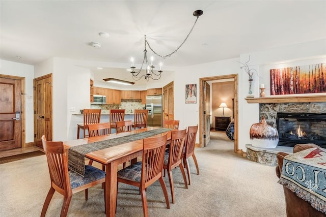 dining area with a chandelier, light colored carpet, and a stone fireplace