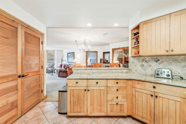 kitchen with light carpet, decorative backsplash, light stone countertops, light brown cabinetry, and a notable chandelier