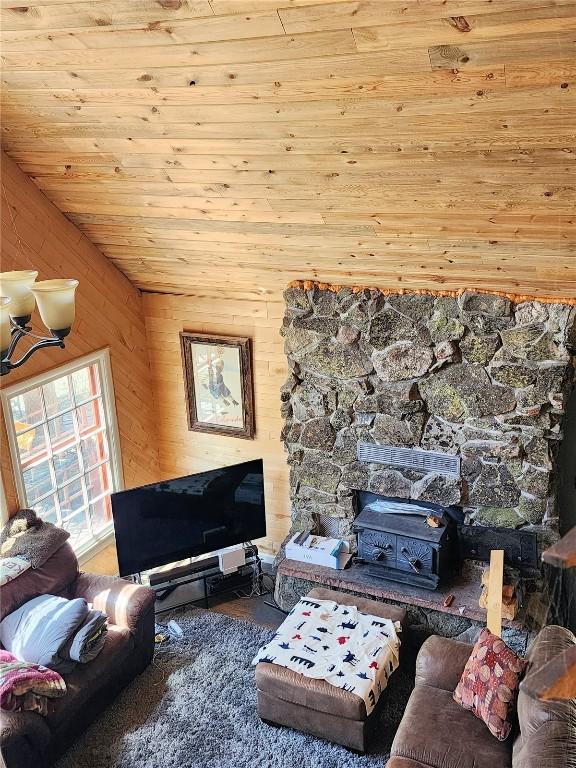 living room with vaulted ceiling, wooden ceiling, a wood stove, and wooden walls