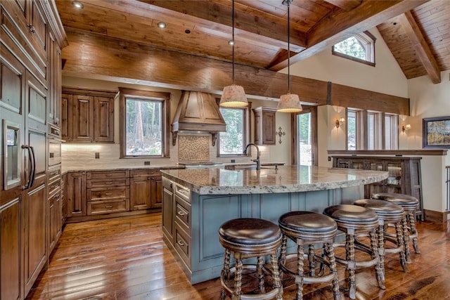 kitchen featuring tasteful backsplash, stainless steel oven, brown cabinets, wooden ceiling, and custom exhaust hood