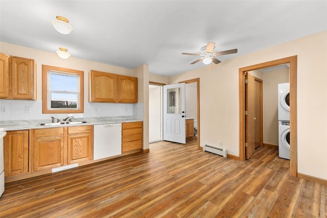 kitchen featuring white dishwasher, ceiling fan, baseboard heating, sink, and stacked washer and clothes dryer