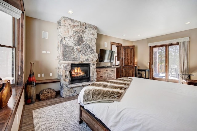 bedroom featuring hardwood / wood-style floors, access to outside, and a stone fireplace