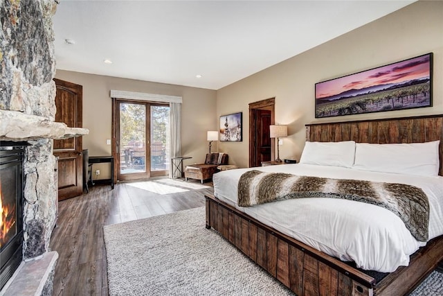 bedroom with access to exterior, wood-type flooring, and a stone fireplace