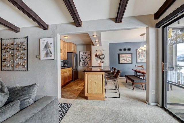 kitchen featuring pendant lighting, beamed ceiling, a breakfast bar area, stainless steel fridge, and light carpet