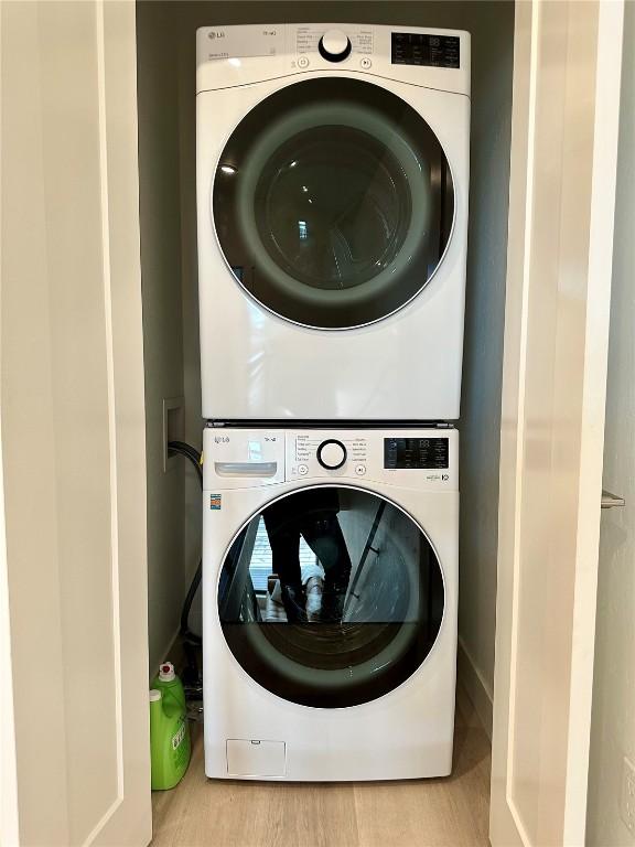 clothes washing area with stacked washer / dryer and light hardwood / wood-style flooring