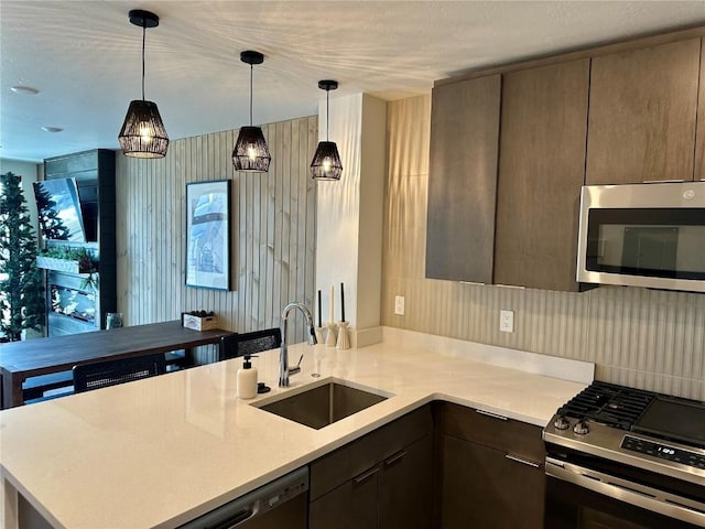 kitchen featuring kitchen peninsula, pendant lighting, stainless steel appliances, and sink