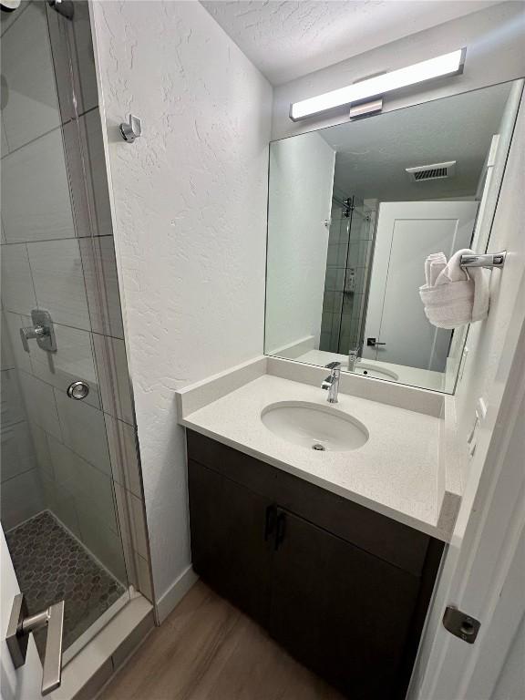 bathroom with a textured ceiling, vanity, wood-type flooring, and walk in shower