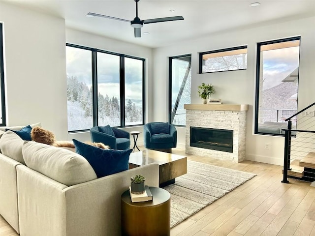 living area with a wealth of natural light, a stone fireplace, light wood-style flooring, and stairs