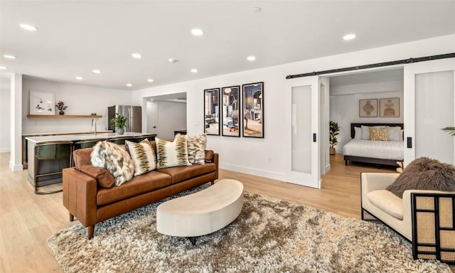 living area featuring light wood-type flooring, a barn door, baseboards, and recessed lighting