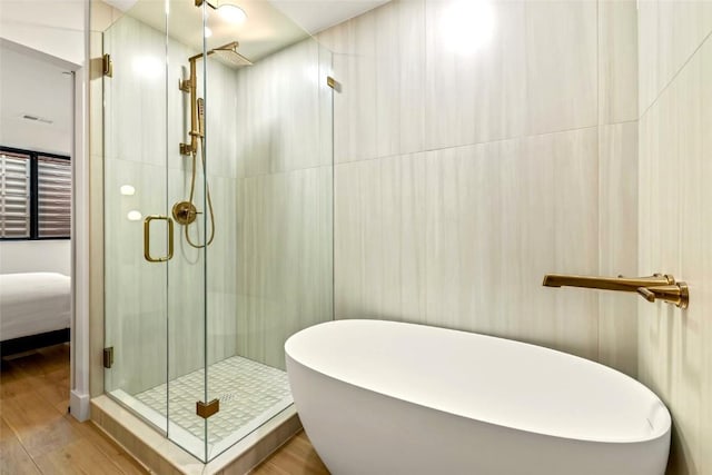 ensuite bathroom featuring a stall shower, ensuite bathroom, wood finished floors, and a soaking tub