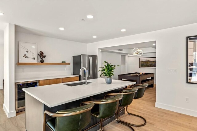 kitchen with light wood-style flooring, wine cooler, light countertops, stainless steel refrigerator with ice dispenser, and a sink