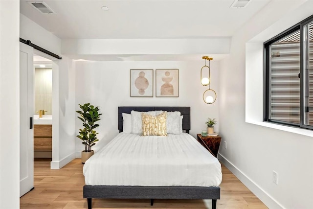 bedroom with a barn door, light wood-type flooring, visible vents, and baseboards