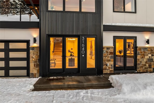 snow covered property entrance with a garage, stone siding, and french doors