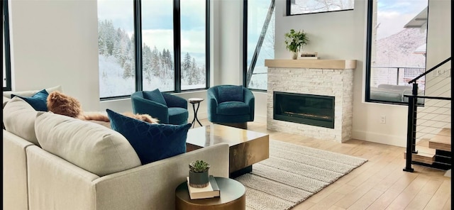 living area with a stone fireplace, stairway, baseboards, and wood finished floors