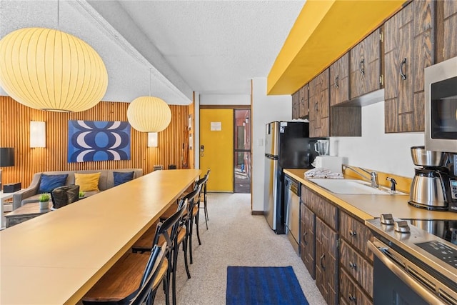 kitchen featuring sink, stainless steel appliances, wooden walls, a textured ceiling, and pendant lighting