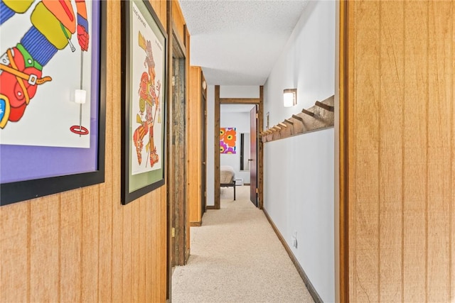 hall with a textured ceiling, light colored carpet, and wooden walls