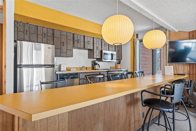 kitchen with decorative light fixtures, a textured ceiling, kitchen peninsula, a breakfast bar area, and appliances with stainless steel finishes