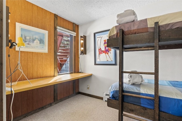 carpeted bedroom featuring wooden walls, a baseboard heating unit, and a textured ceiling