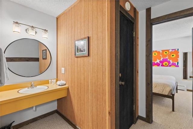 bathroom with sink, wood walls, a textured ceiling, and a baseboard heating unit