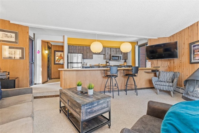 living room featuring a baseboard heating unit, wood walls, a textured ceiling, and light colored carpet