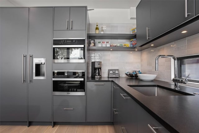 kitchen with sink, light hardwood / wood-style flooring, stainless steel refrigerator with ice dispenser, backsplash, and black double oven