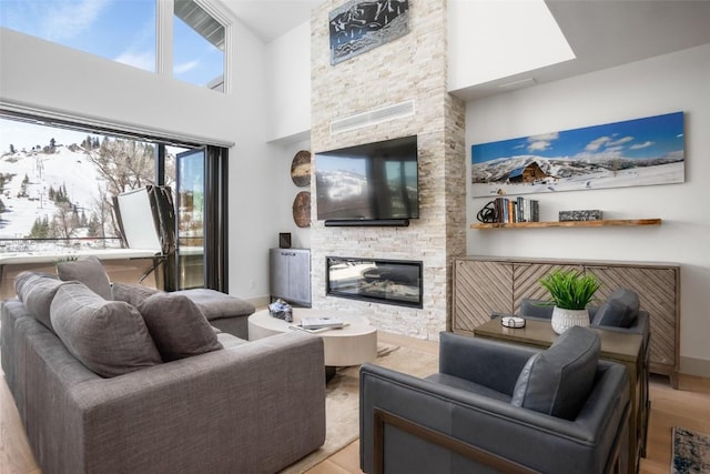 living room with light hardwood / wood-style floors, a stone fireplace, and a high ceiling