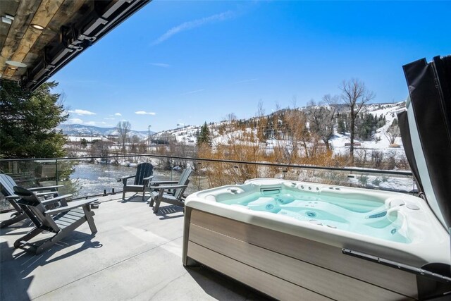 snow covered patio featuring a mountain view and a hot tub